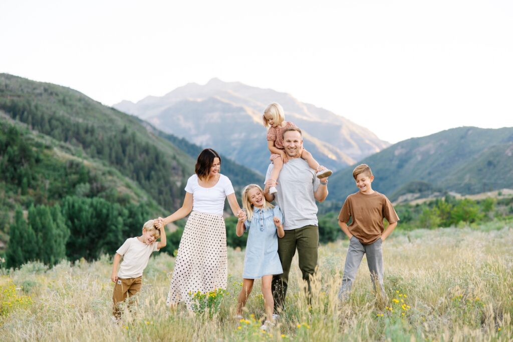 Family walking together through field with mountains behind. Mary Horne Nelson | Provo Family Photographer